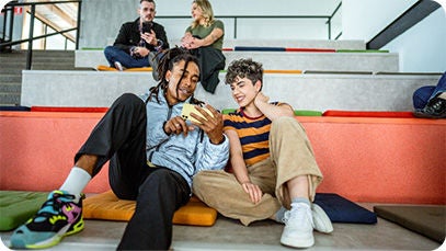 Quatre personnes : deux sont assises sur un grand escalier en arrière-plan et deux sont assises au premier rang. Les deux couples utilisent un téléphone.