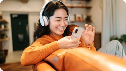 Une personne portant un casque, assise sur un canapé orange, qui utilise un téléphone portable.